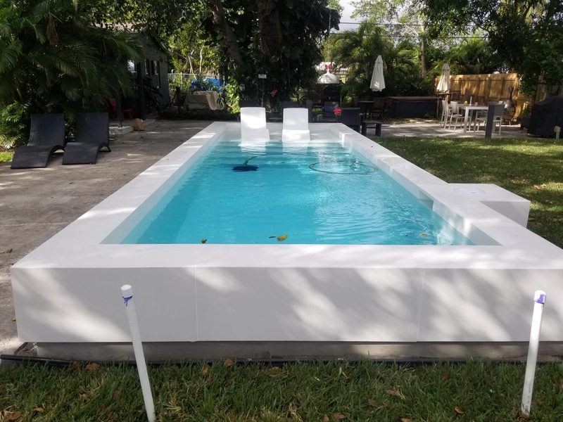 Just-completed modern pool with white deck and glass tile in Naples